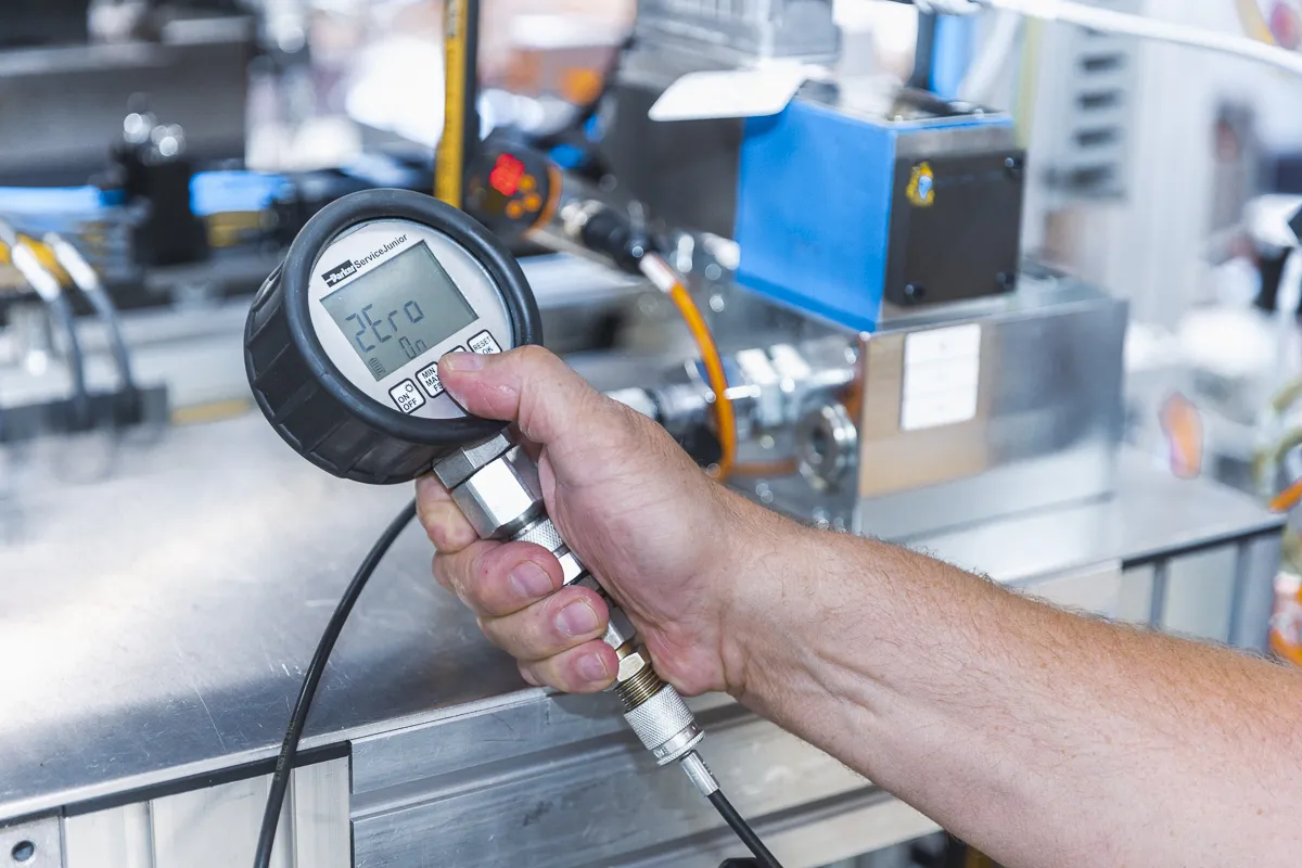 Hand hält Messmaschine vor Industriemaschine in der Hand