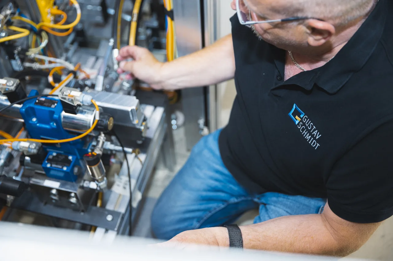 Gustav-Schmidt-Mitarbeiter sitzt neben Maschine und arbeitet an dieser