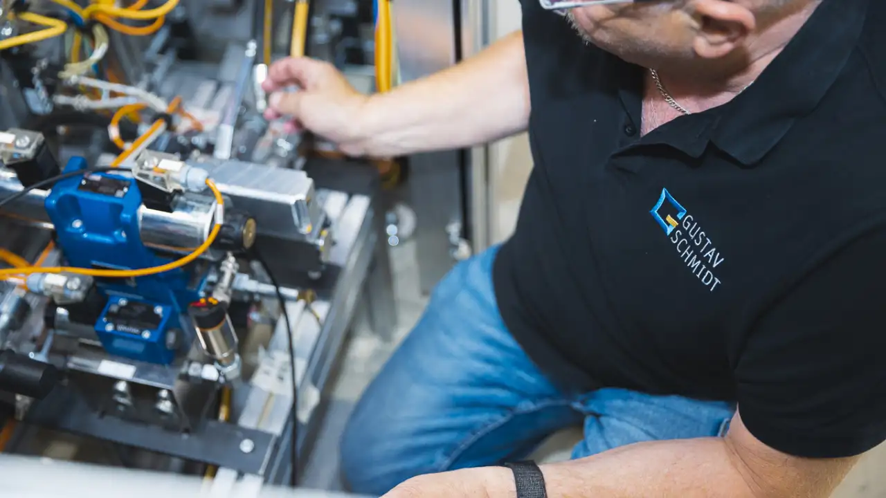 Gustav-Schmidt-Mitarbeiter sitzt neben Maschine und arbeitet an dieser
